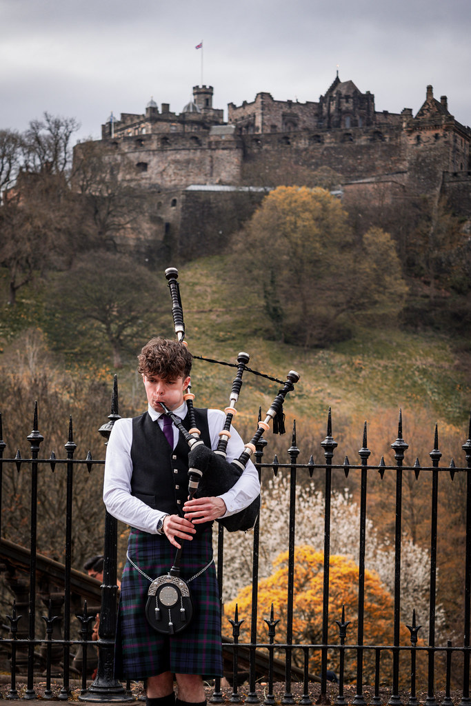 Bagpiper performing with Edinburgh Castle on the hill behind him