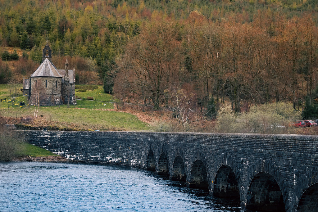 Long stone bridge crossing a reservoir beside autumn woodland in Wales