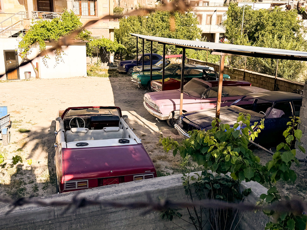 Red and pink vintage convertible cars parked in a sunlit courtyard in Turkey