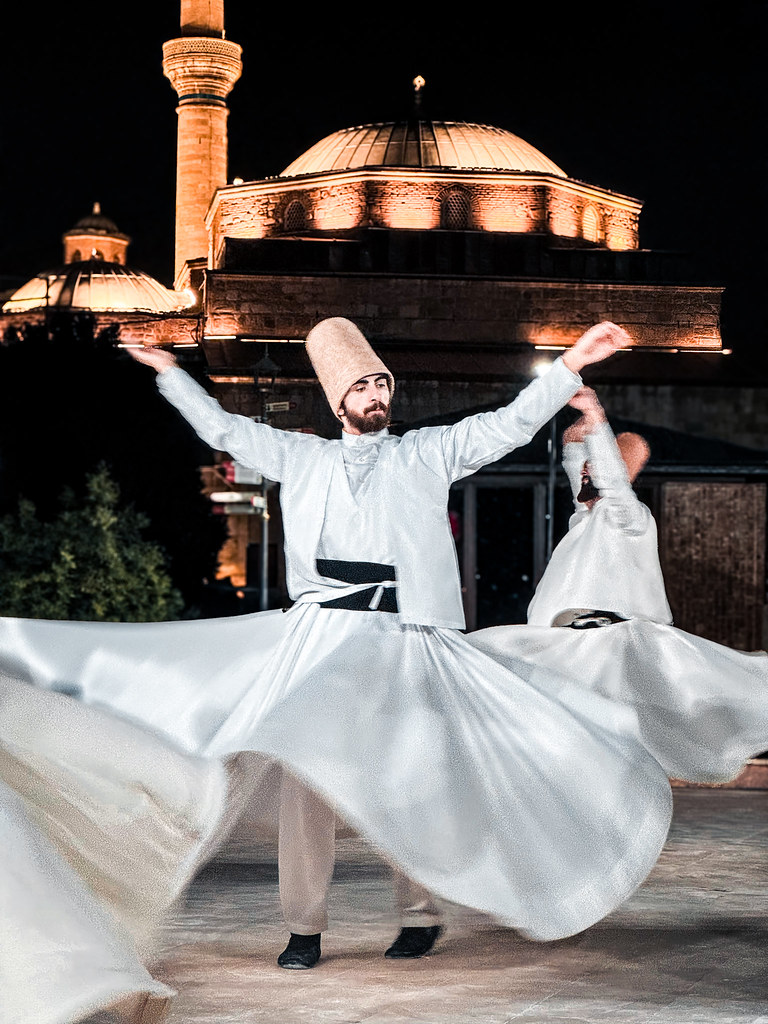 Whirling dervishes performing at night beside an illuminated mosque
